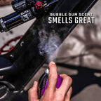 Person using a purple spray can to freshen up a car interior with text 'Bubble Gum Scent Smells Great'.