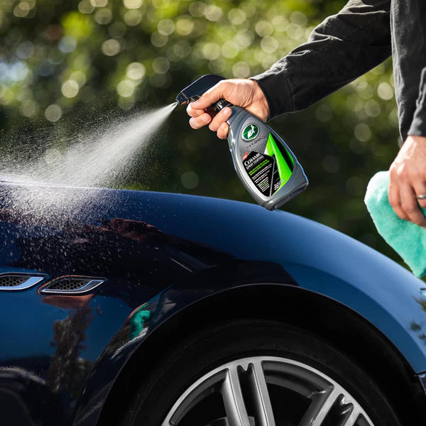 Person cleaning a car with a spray bottle and towel, with a blurred green background
