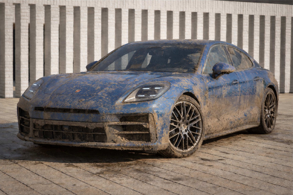 Muddy blue sports car on a wooden surface with a brick wall background