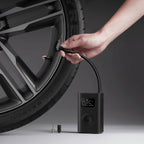 Hand using a digital tire inflator to inflate a car tire on a gray background