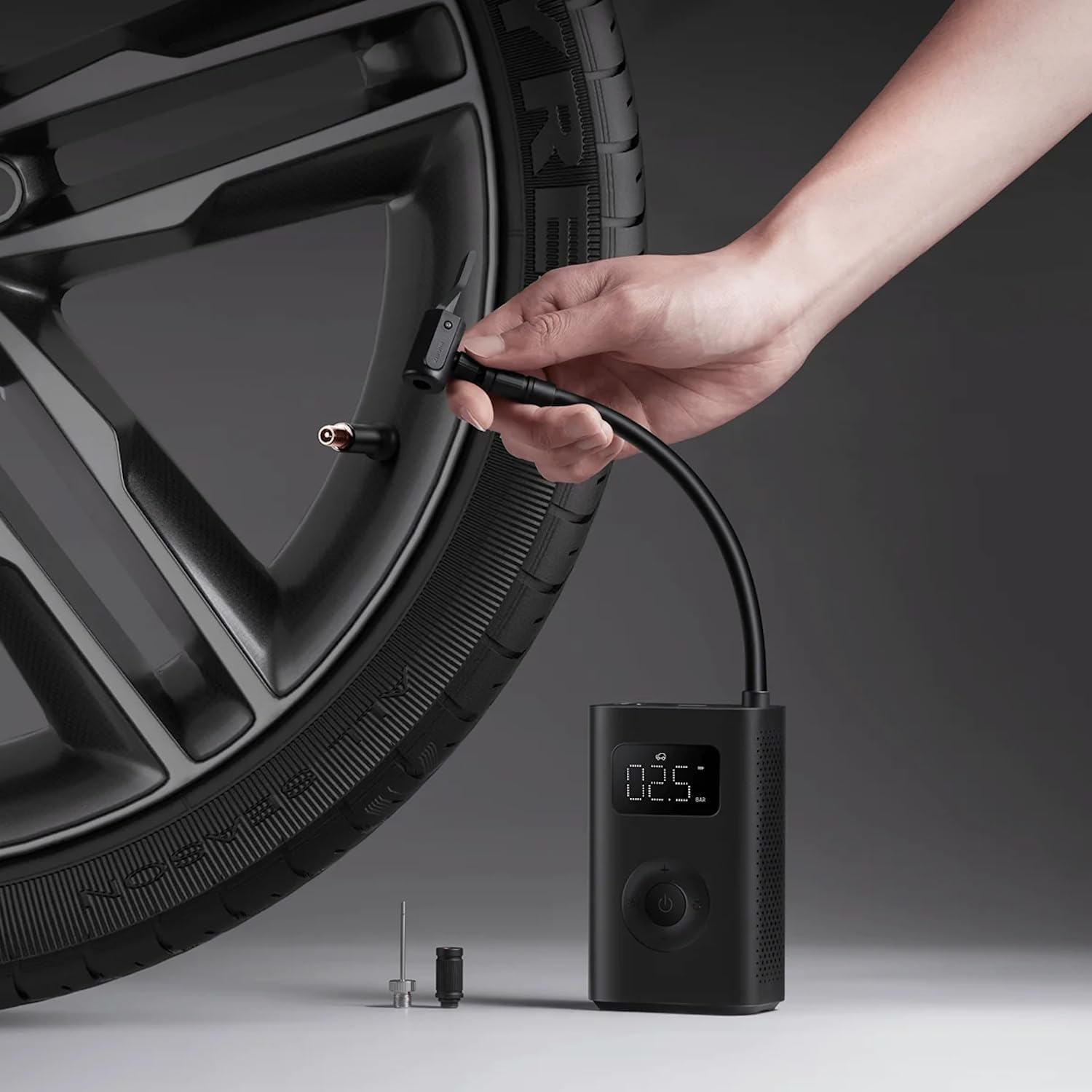 Hand using a digital tire inflator to inflate a car tire on a gray background
